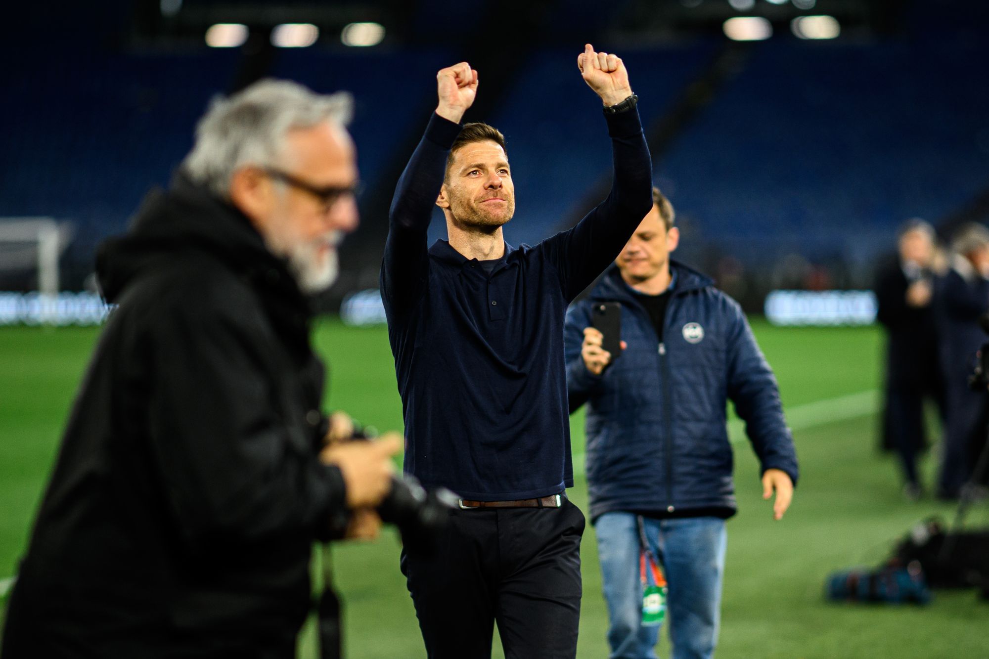 Xavi Alonso steht auf dem Fußballplatz und reckt die Arme in die Luft.