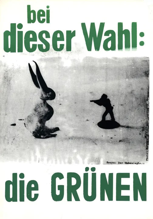 Grüne Schrift, die sagt "bei dieser Wahl: die Grünen". In Grau sieht man ein Kaninchen, auf das ein Spielzeugsoldat mit einem Gewehr zielt.