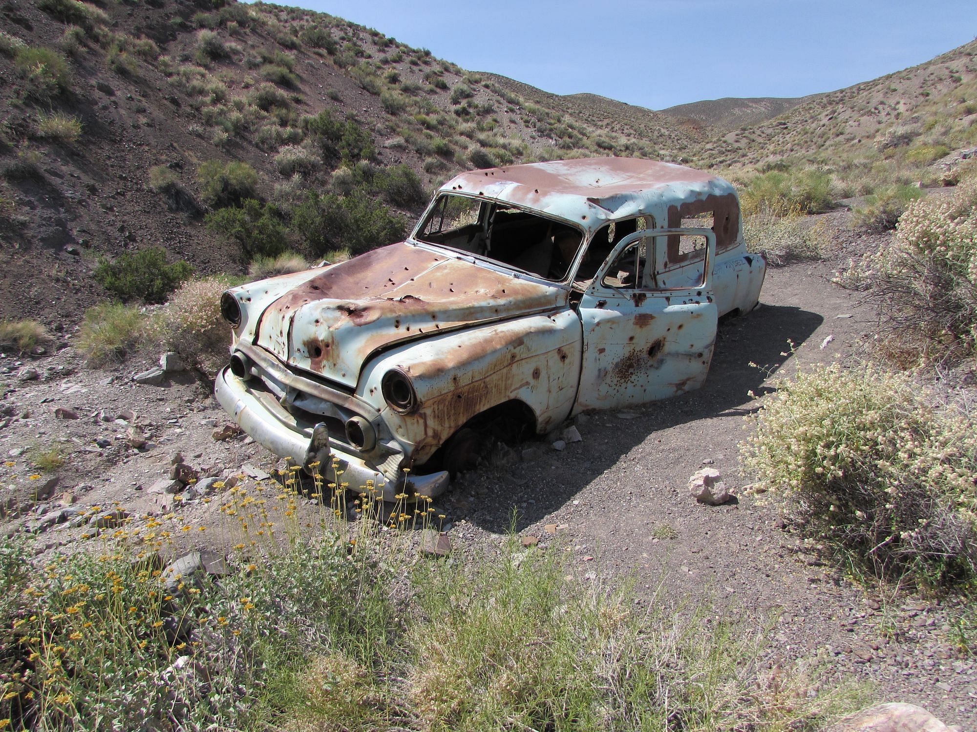 Ein verlassenes Auto im Death Valley. Es ist rostig und mit Einschusslöchern übersäht.