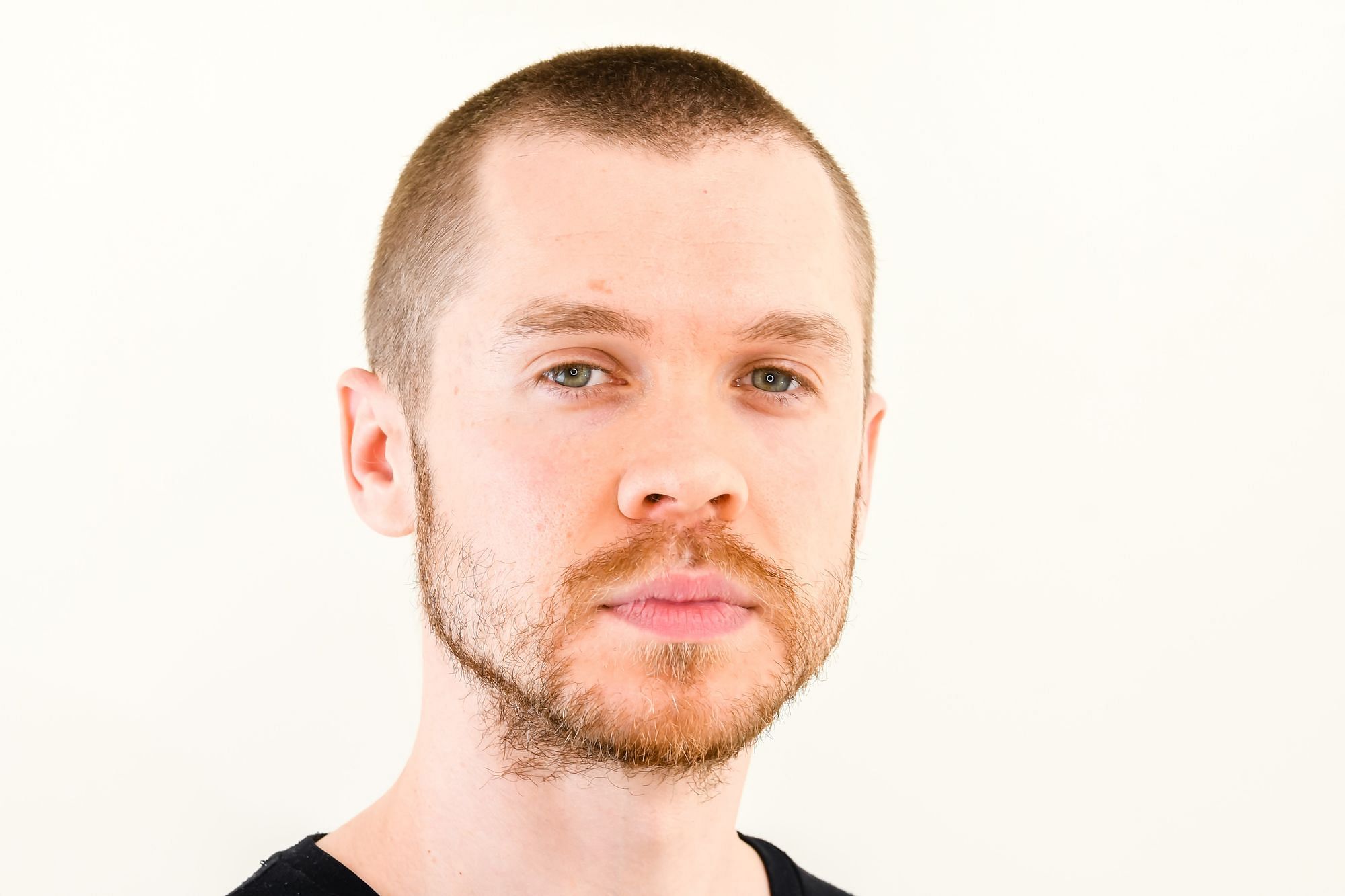 Ein Mann Mitte 30 mit kurzen Haaren und Drei-Tage-Bart vor einem weißen Hintergrund