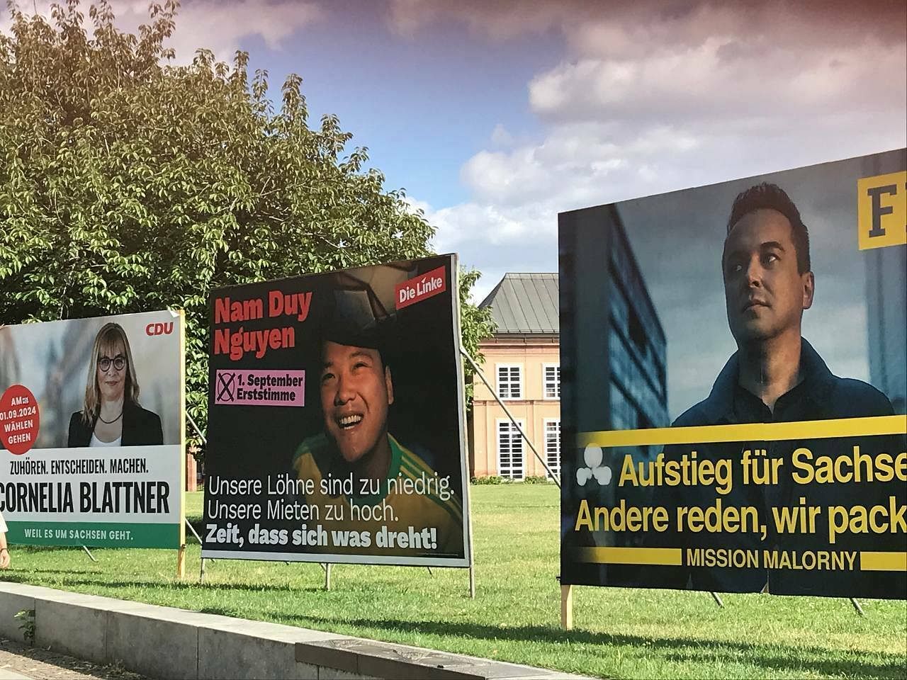 Drei große Wahlplakate. In der Mitte steht das Plakat der Linken mit einem Bild von Nam Duy Nguyen.