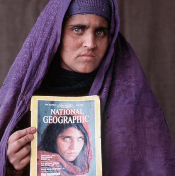 Sharbat Gula blickt in die Kamera und hält eine Ausgabe des National Geographic in der Hand, auf der sie selbst abgebildet ist.