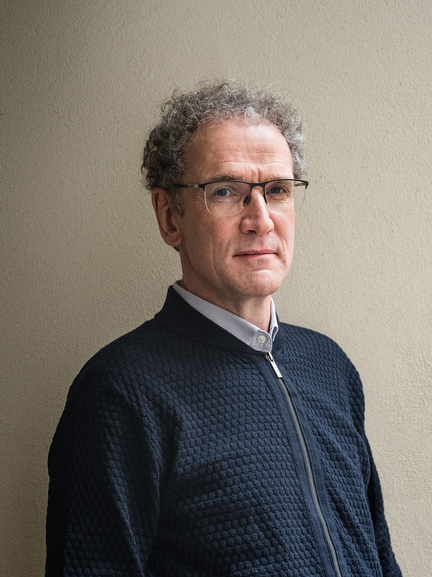 Ein Bild von Dirk Oschmann, einem Mann mit grauen kurzen Locken, einer halb-randlosen Brille und einer Strickjacke.