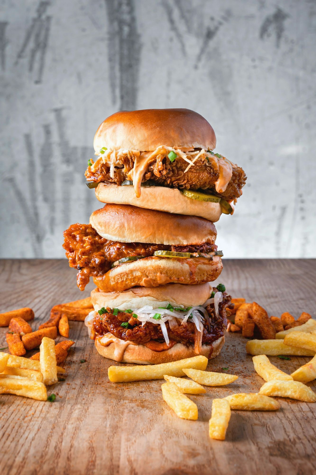 Ein mehrstöckiger Burger. Soße läuft aus ihm heraus. Davor sind Pommes verteilt.
