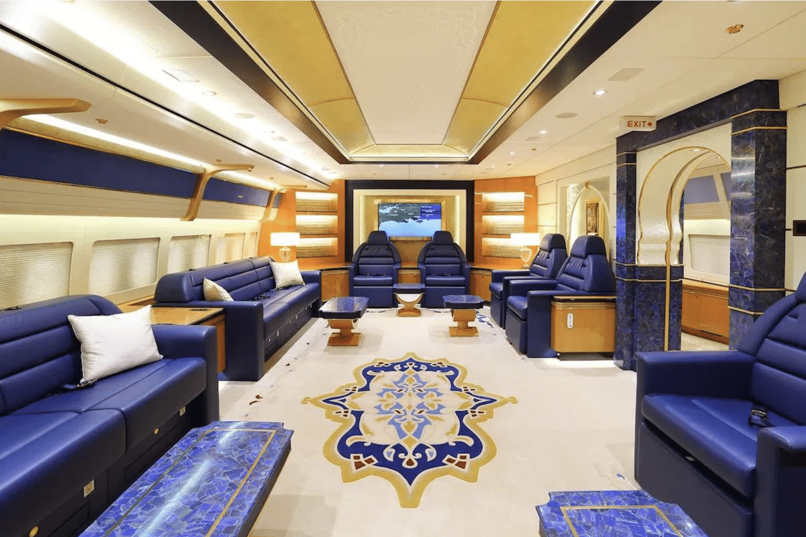 Auf dem Bild ist das Innere eines Flugzeugs zu sehen, mit breiten blauen Sesseln, goldenen Wänden und Teppichboden.