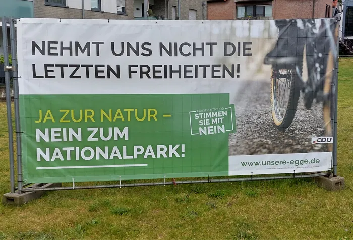 Auf einem Transparent steht: "Nehmt uns nicht die letzten Freiheiten! Ja zur Natur - nein zum Nationalpark!". Dazu ist ein Radfahrer abgebildet.