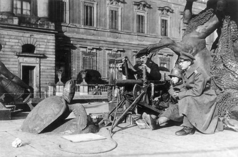 Revolutionäre Soldaten mit Maschinengewehr in Stellung vor dem Berliner Stadtschloss, November 1918. Drei bewaffnete Männer in Militärmänteln und Stahlhelmen bedienen ein MG hinter einer improvisierten Deckung. Die klassizistische Schlossfassade bildet den Hintergrund.