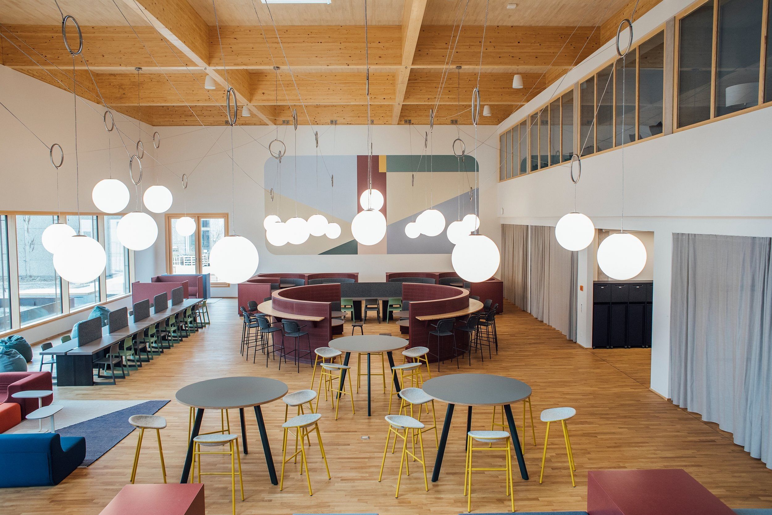 Ein Foto eines Co-Working-Spaces mit Stehtischen, Hockern, Arbeitsplätzen. Im Raum hängen viele runde Lampen, es gibt eine große Fensterfront.