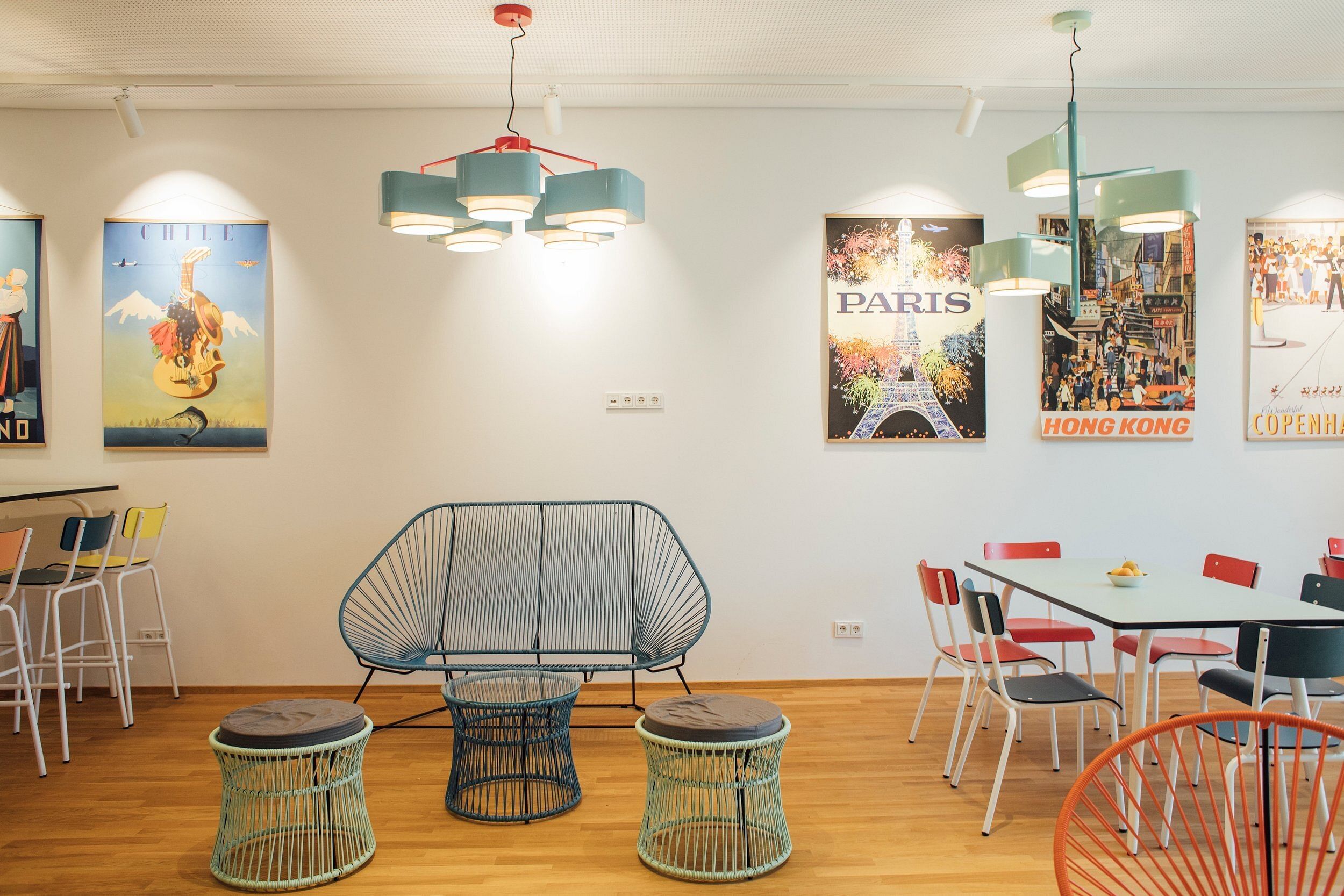 Ein Foto aus dem Café der Alemannenschule mit Tischen, Stühlen, Bänken. An der Wand hängen Plakate. Der Raum ist warm beleuchtet und bunt.