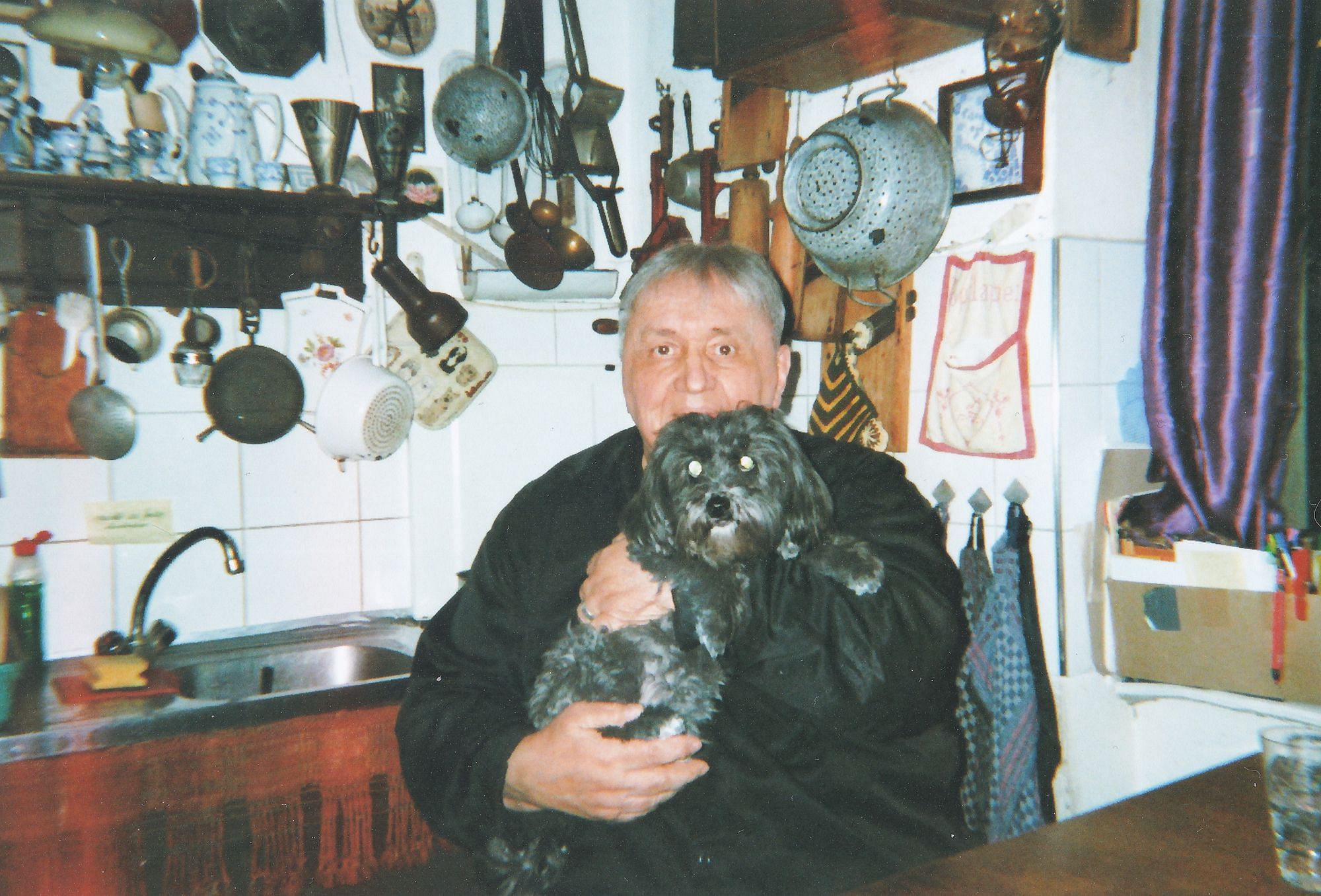 Curt hält seinen Hund auf dem Arm. Er sitzt in der Küche.