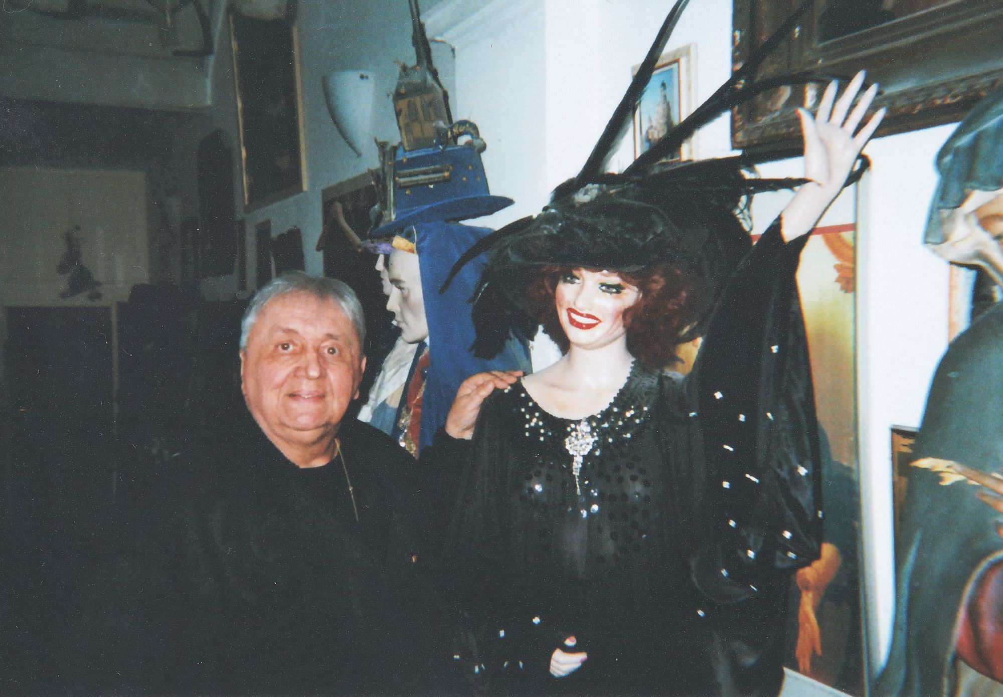 Curt steht neben einer Puppe, die ein schwarzes Kleid und einen Hut trägt.