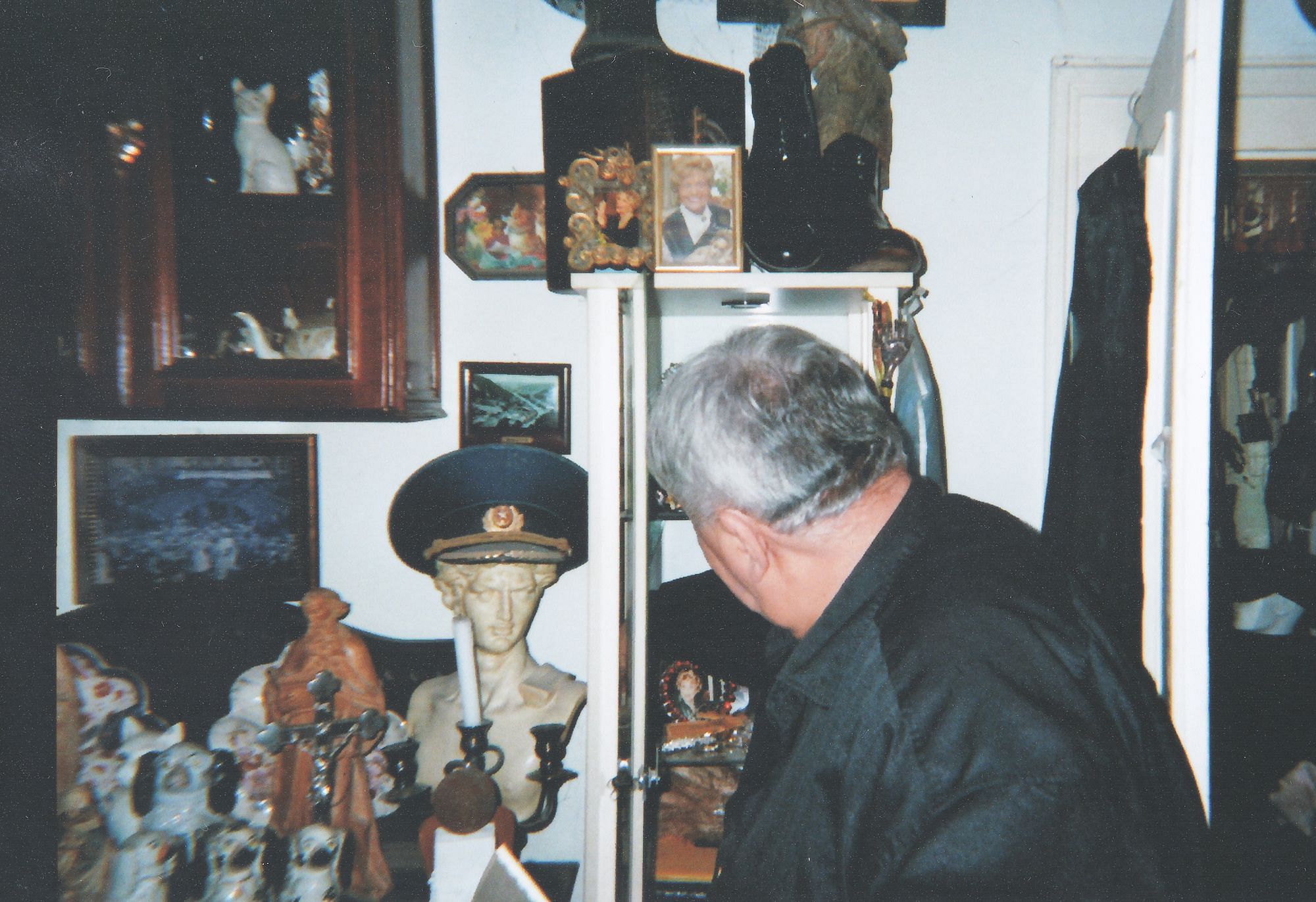 Curt blickt auf eine Vitrine. An der Wand hängen viele verschiedene Gegenstände.