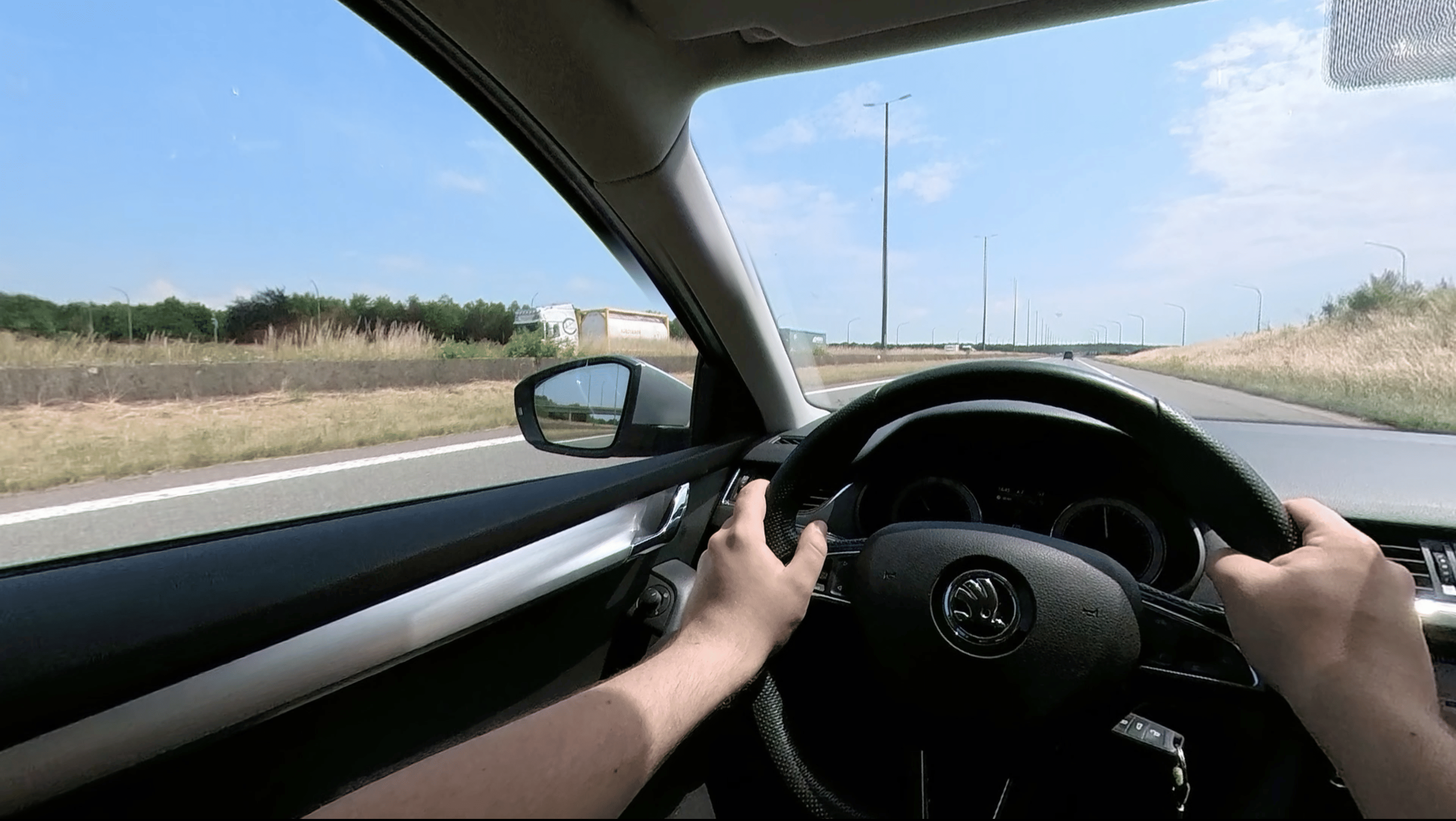 Die Sicht eines Autofahrers. Er befindet sich auf einer Schnell- oder Landstraße. Hände halten ein Lenkrad fest.