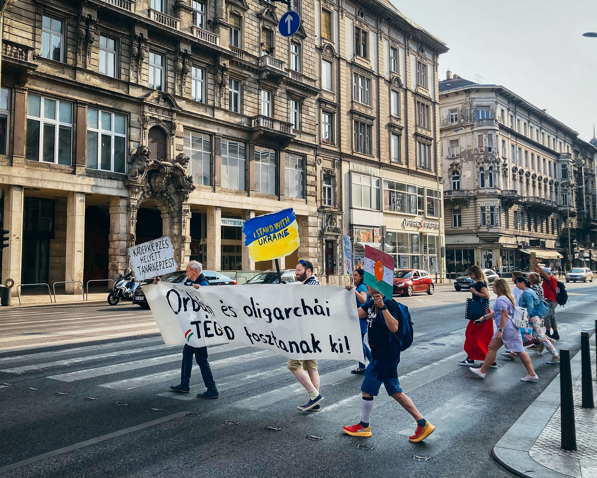 Eine Gruppe Menschen läuft auf einen Zebrastreifen, sie tragen ein Transparent und haben Schilder in den Händen.