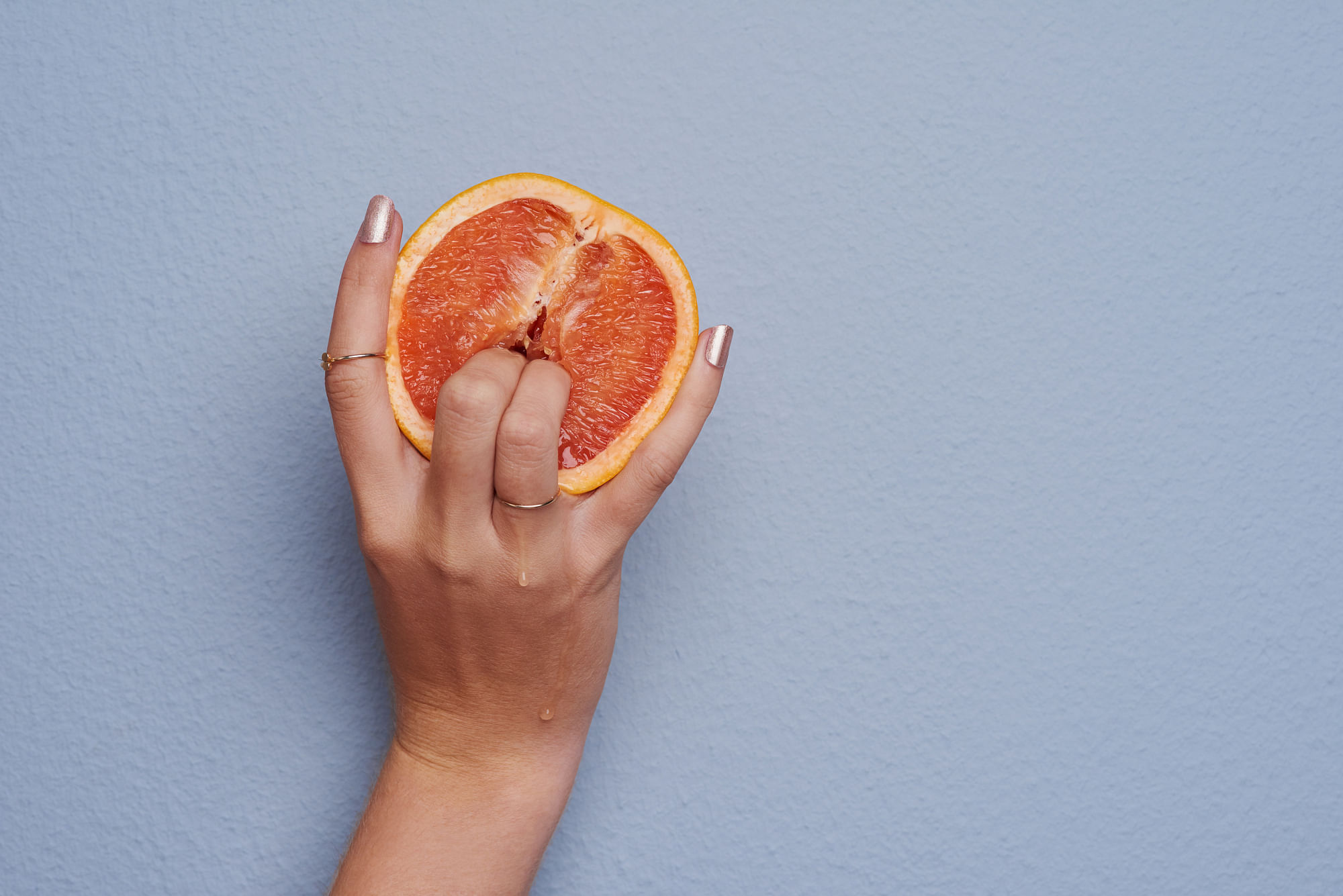 Zwei manikürte Finger bohren sich in eine halbe Grapefruit.