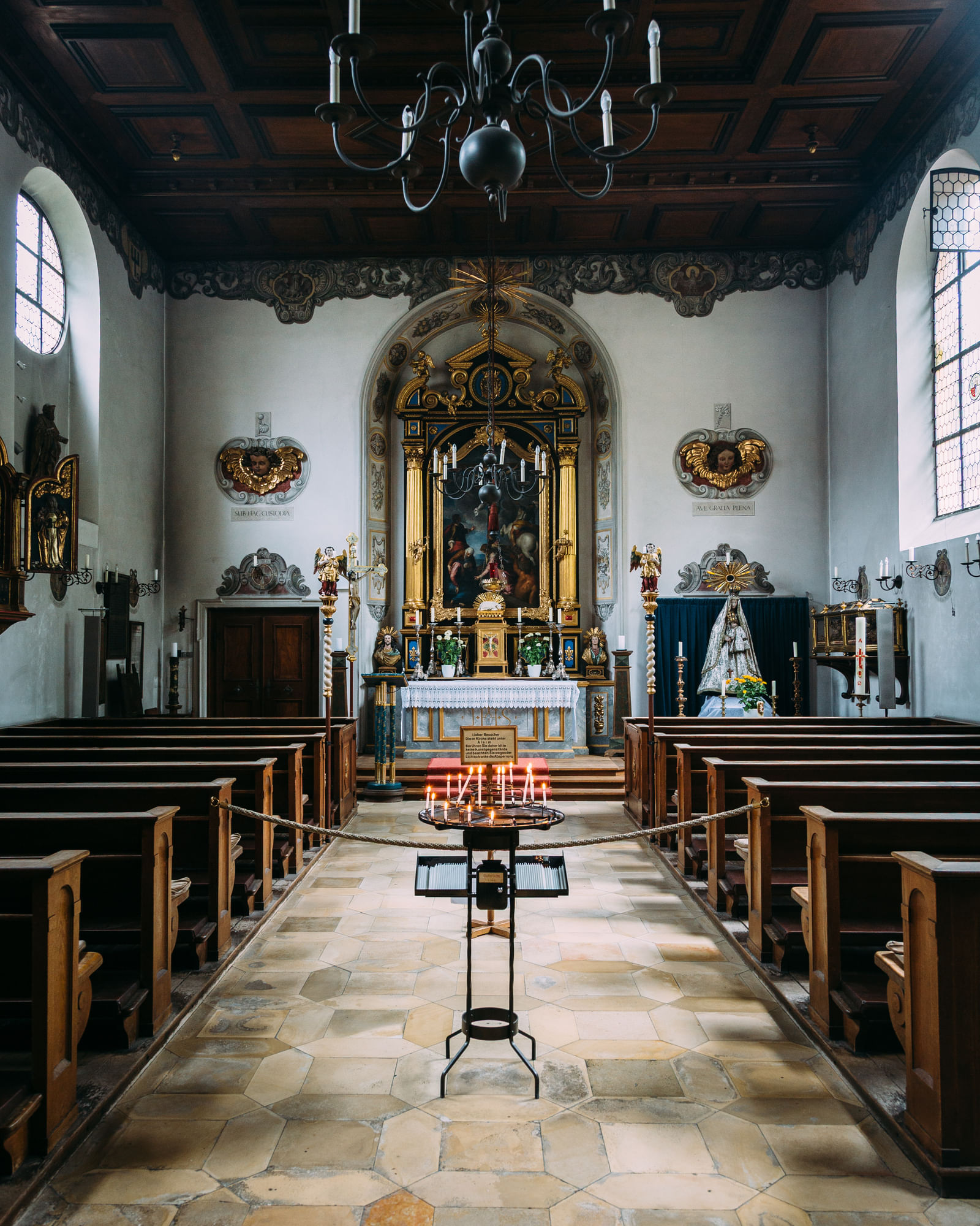 Eine Kirche mit prunkvollem Altar. Weiter vorne im Gang sieht man Kerzen brennen.
