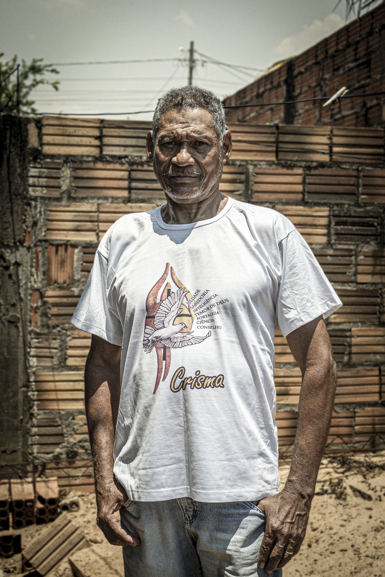 Ein Mann in weißem T-Shirt blickt in die Kamera, die Hände in den Hosentaschen.